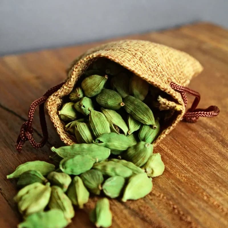 Whole green cardamom pods spilling from a jute export bag
