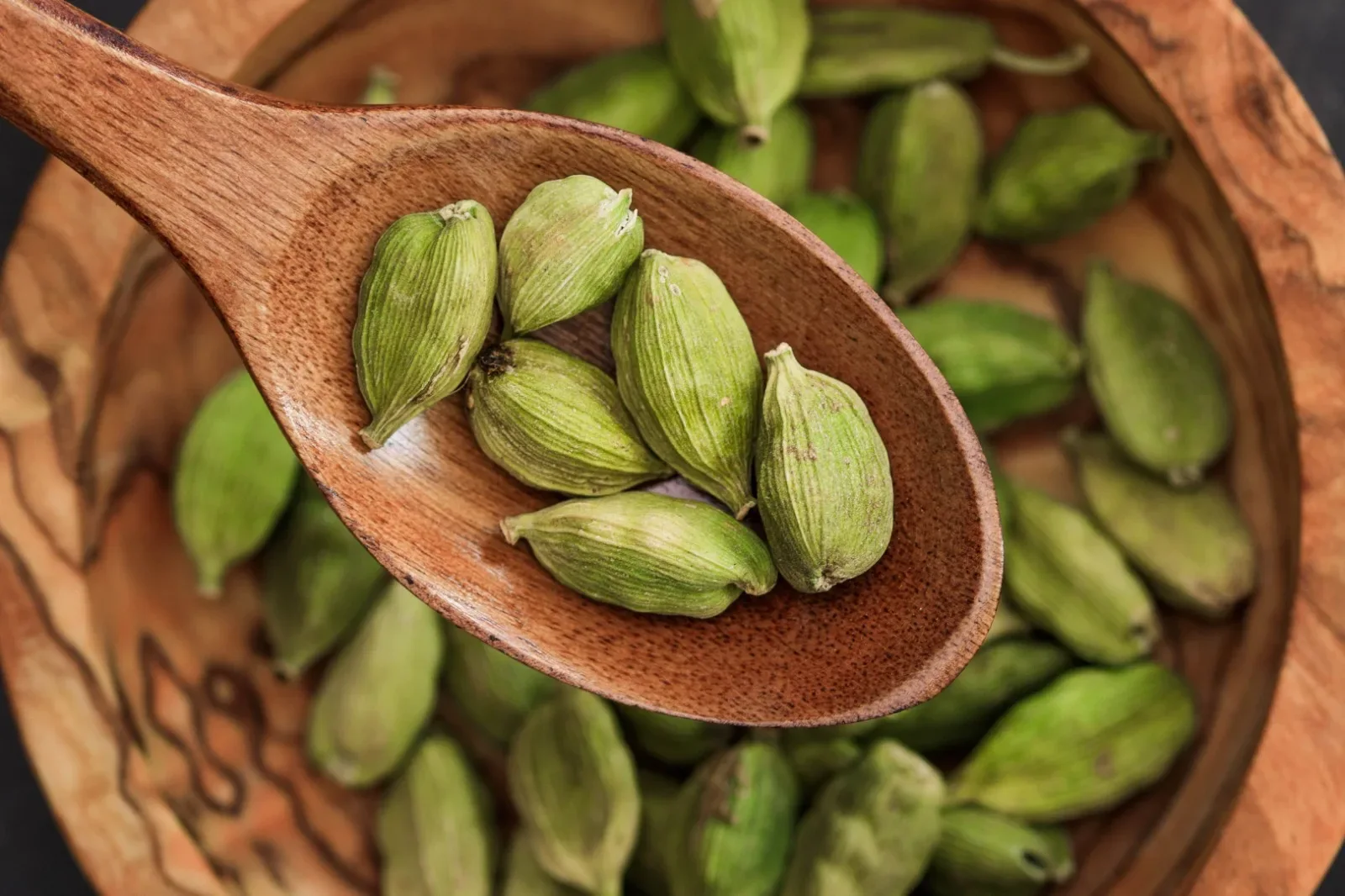 Wooden scoop of calibrated green cardamom pods
